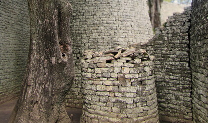 A round stone tower next to a tree, flanked on all sides by stone walls